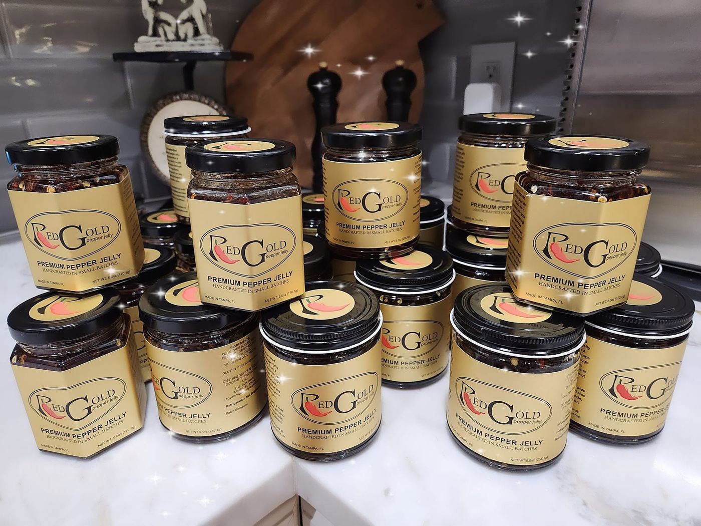 Jars of RedGold pepper jelly with gold labels stacked on a kitchen counter